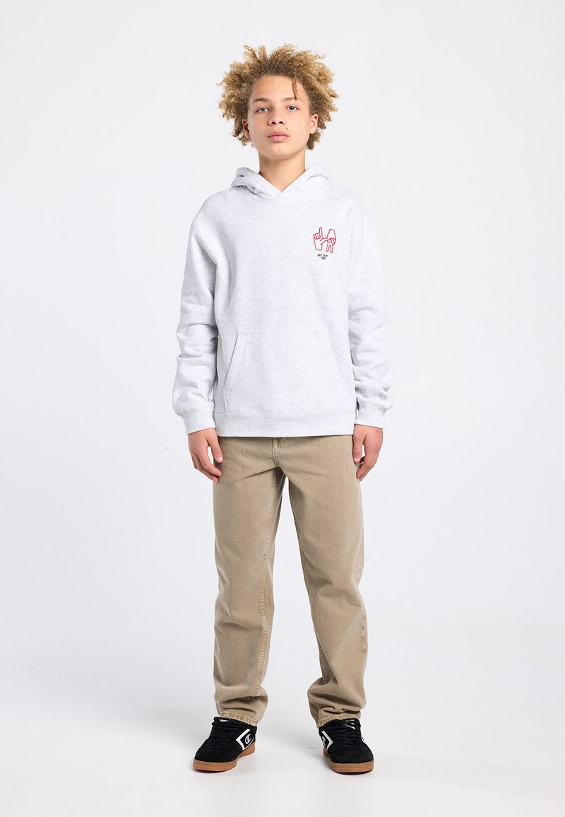 Lichtgrijze hoodie met voorzak in kangaroostijl, voorzien van een rode afbeelding op de linkerborst. Gecombineerd met beige broek en zwarte schoenen.