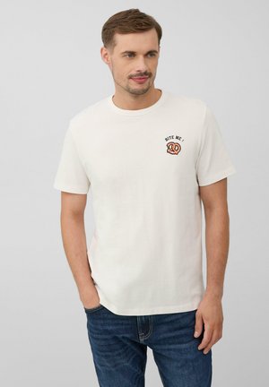 T-shirt en coton beige clair avec col rond, manches courtes et un petit graphique de bretzel avec le texte "MANGE-MOI !" sur le devant. Coupe décontractée.