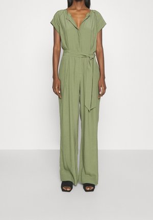 Olijfgroene jumpsuit met korte mouwen, V-hals, ceintuur in de taille en wijde pijpen. De stof lijkt lichtgewicht met een gladde textuur.