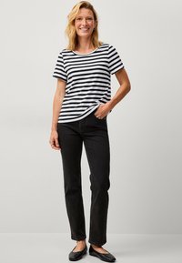 Zwart-wit gestreepte t-shirt met een ronde hals, gecombineerd met zwarte rechte jeans en zwarte flat shoes. Model staat met één hand in de zak.
