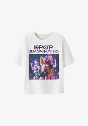 Camiseta blanca de manga corta con gráfico colorido de tres personajes femeninos animados y texto "KPOP DEMON HUNTERS" encima de ellos.