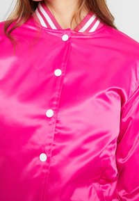 Hot pink satin bomber jacket with white snap buttons and a striped ribbed collar. Smooth texture and casual design.