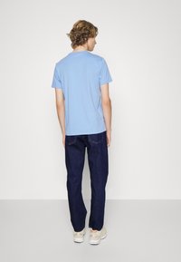 T-shirt en coton bleu clair à manches courtes, associé à un jean foncé. Coutures visibles et coupe décontractée. Les chaussures sont des baskets de couleur claire.