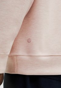 Sudadera de color rosa claro con una textura suave, dobladillo redondeado en la parte inferior y un pequeño logotipo en un tono a juego cerca de la costura.