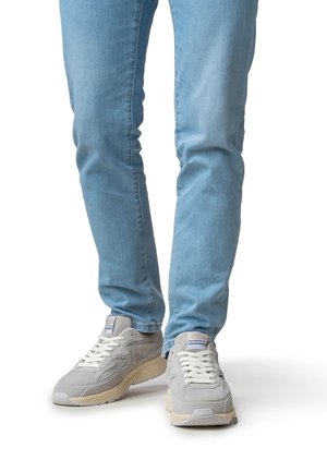 Light gray sneakers with textured suede and mesh upper, white laces, and cream midsole, paired with light blue fitted jeans.