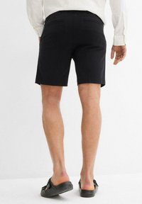 Shorts neri con una vestibilità su misura, dotati di due tasche posteriori e un finish pulito. Abbinati a scarpe nere senza lacci.