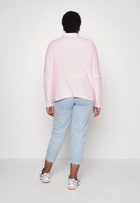 Pull à maille côtelée rose clair avec une coupe décontractée, porté par-dessus un jean en denim bleu clair, associé à des chaussures de sport blanches et noires.