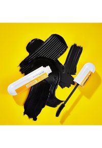 Des tubes de mascara avec des accents blancs et oranges sur un fond de coups de pinceau noirs brillants et une surface jaune vif.