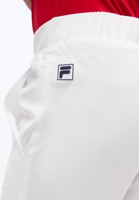 Κοντινή λήψη λευκού παντελονιού με ελαστική μέση και πλαϊνή τσέπη, με μικρό μαύρο και άσπρο λογότυπο "F" κοντά στην τσέπη.