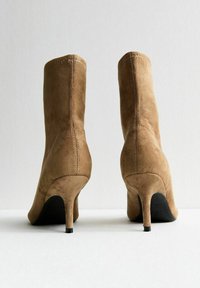 Bottines en daim beige avec une silhouette ajustée, un bout pointu et des talons aiguilles de 10 cm. Présentent des coutures visibles et une finition texturée.