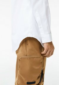 Witte longsleeve shirt met knoopmanchetten, gecombineerd met bruine cargobroek met een ritszak en textuurstof.