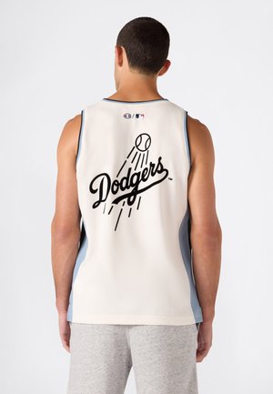Mann trägt weißes ärmelloses Dodgers-Sporttrikot mit schwarzem Text und Baseball-Grafik auf dem Rücken, kombiniert mit hellgrauen Shorts.
