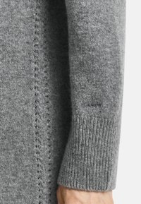 Grijze gebreide sweater mouw met een geribbelde manchet en delicate zijnaaddetails. Zachte textuur met een subtiel, gelijkmatig patroon.