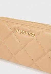 Beżowy pikowany skórzany portfel z złotym zamkiem błyskawicznym i wytłoczonym logo "Valentino". Wzór o fakturze z diamentowymi kształtami.