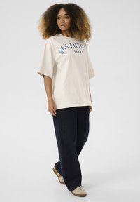 T-shirt beige oversize avec "SAN ANTONIO TEXAS" imprimé en bleu et pantalon navy ample. Matériau en coton doux, design décontracté.