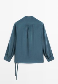 Blågrøn langærmet bluse med plisseret rygdetalje, rundet krave og manchetter med knapper. Har bindebånd ved kanten for justerbar pasform.