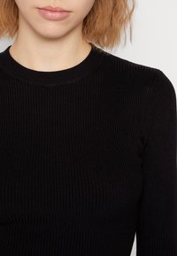 Schwarzes geripptes Strickoberteil mit rundem Halsausschnitt und tailliertem Design. Der Stoff hat ein strukturiertes Aussehen mit vertikalen Linien.