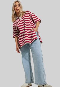 Roter und beiger gestreifter, übergroßer Oberteil mit kurzen Ärmeln, kombiniert mit hellblauen weit geschnittenen Jeans und weißen Sneakers. Glatte Stofftextur.