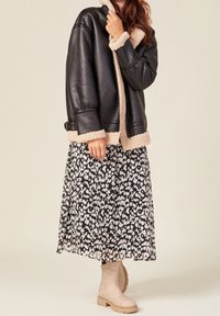 Black faux leather jacket with beige shearling lining, paired with a black and white patterned maxi skirt and beige ankle boots.