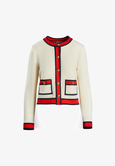 Krema pletena kardigana z rdečimi in mornarsko modrimi akcenti, pet zlatih gumbov in dvema sprednjima žepoma s kontrastnim obrobami.