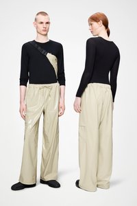 Μαύρο μακρυμάνικο τοπ με μια μεγάλη πλαϊνή τσέπη σε συνδυασμό με λαμπερό, μπεζ παντελόνι με ελαστική μέση και τσέπες cargo. Μαύρα παπούτσια.