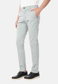 Chino grigi chiari realizzati in tessuto misto cotone, con una vestibilità slim, tasche frontali e chiusura a bottone. Indossati con scarpe nere.