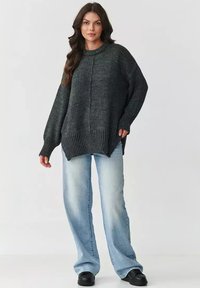 Przesadzony sweter w kolorze węgla z dzianiny, z prążkowanymi mankietami i dołem, noszony z jasnoniebieskimi spodniami o szerokich nogawkach i czarnym obuwiem.