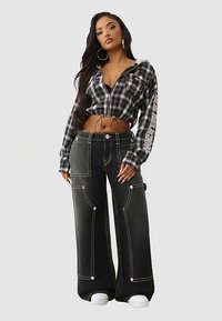 Czarna i biała krótka koszula z zamkiem na przodzie i długimi rękawami; spodnie czarne o wysokim stanie i szerokich nogawkach z kontrastowymi białymi przeszyciami i kieszeniami.