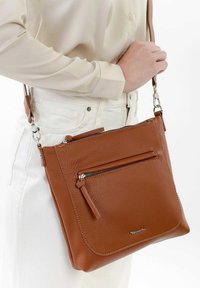 Braune Leder-Crossbody-Tasche mit strukturiertem Finish, ausgestattet mit einer Frontreißverschlusstasche und einem verstellbaren Tragegurt mit silbernen Beschlägen.