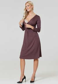 Long-sleeve, deep V-neck dress in muted mauve fabric, cinched at the waist, flaring below the knee, paired with black high heels.