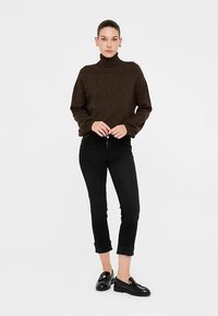 Brauner Rollkragenpullover mit dezenten Glitzereffekten, kombiniert mit schwarzen, schmal zulaufenden Jeans und schwarzen Loafers, mit einfachem Design und umgeschlagenen Säumen.