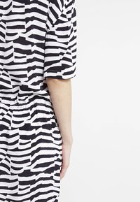 Vêtement à manches courtes rayé noir et blanc avec ceinture élastique, présentant des largeurs de rayures variées et une texture de tissu lisse.