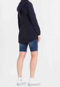 Granatowa, lekka kurtka z kapturem, długimi rękawami i asymetrycznym dołem. Połączona z dżinsowymi szortami i białymi, wysokimi trampkami.