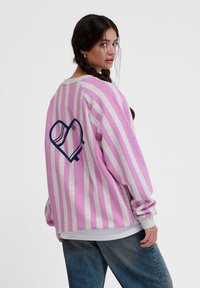 Ljusrosa och vita randiga sweatshirt med en grafisk hjärtdesign på baksidan. Har en avslappnad passform och ribbade manchetter.