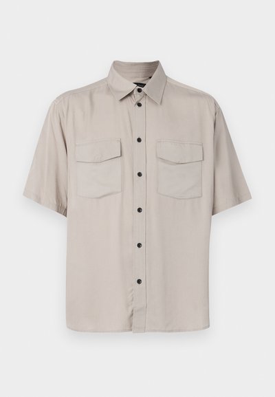 Srajca s kratkimi rokavi v svetli bež barvi z gumbom in ovratnikom, dvema žepoma s poklopcem ter črnimi gumbi spredaj. Gladka, netexturirana tkanina.