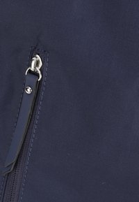 Bolsillo con cremallera de tela azul marino, con un tirador de cremallera de metal plateado y una correa de acento negra, que presenta un material texturizado y detalles de costura.