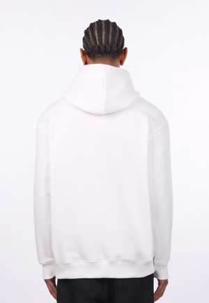 Weißer Kapuzenpullover mit lockerem Schnitt, gerippten Bündchen und Saum sowie einem strukturierten Material; sichtbare Nähte entlang der Schultern.
