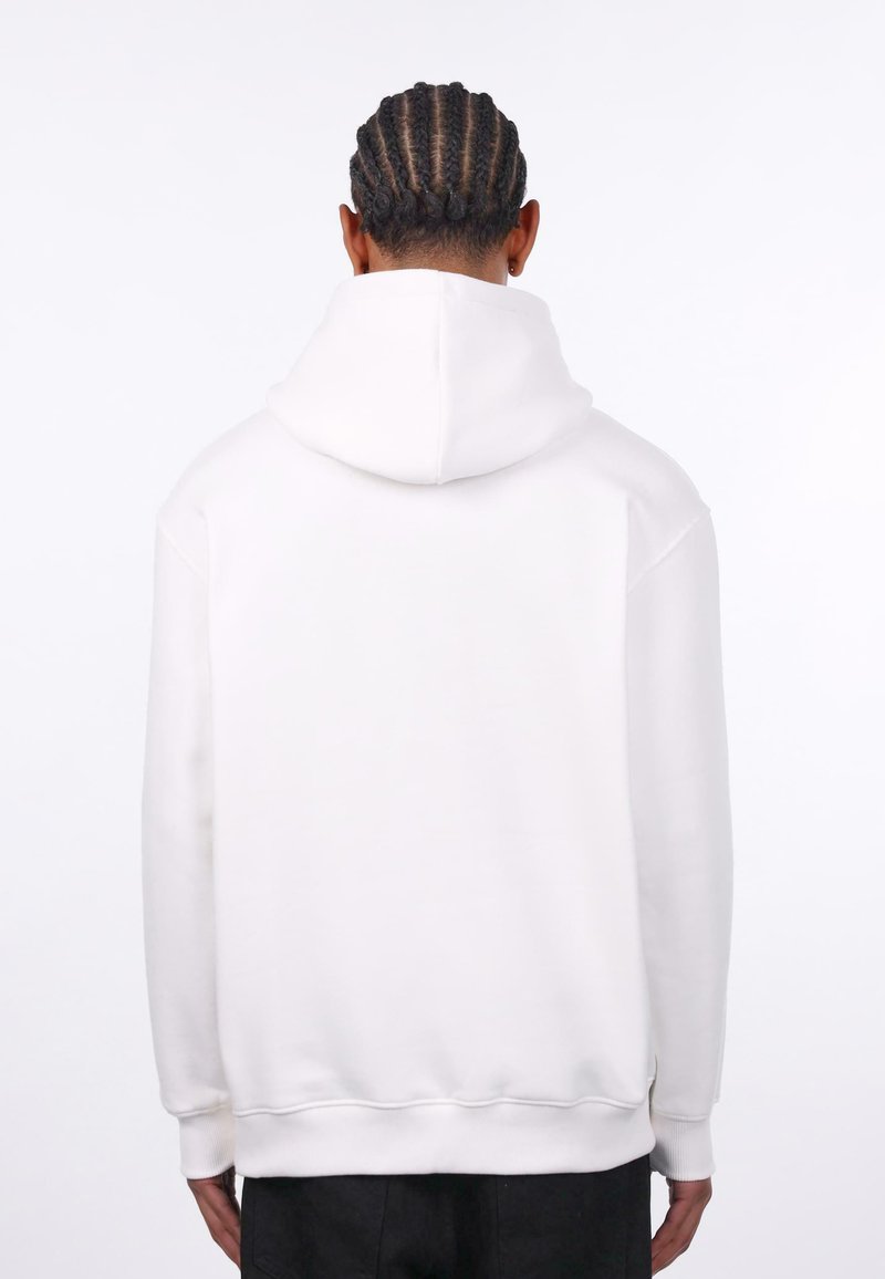 Hvid hættebluse med en afslappet pasform, ribbede cuffs og kant, samt et tekstureret materiale; synlige syninger langs skuldrene.