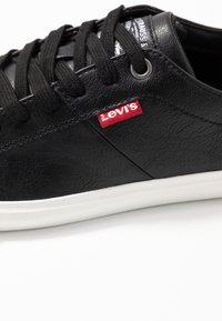 Sneaker in pelle nera con chiusura a lacci, suola in gomma bianca, etichetta rossa con logo Levi's, superficie testurizzata e occhielli rinforzati.
