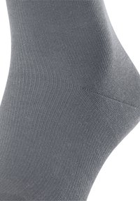 Calzino grigio con una texture liscia e un design a costine, con una tonalità leggermente più scura sul tallone. Il tessuto è elastico e morbido.