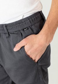 Pantalones cortos gris de cintura elástica con bolsillos laterales en una tela suave. Presenta una pequeña etiqueta de la marca en la cinturilla. Textura suave, diseño casual.