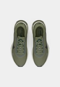 Ζεύγος ελιάς πράσινα παπούτσια τρεξίματος Nike με μαύρα λογότυπα Swoosh, κορδόνια και άσπρες ενδιάμεσες σόλες, σε θέα από πάνω σε λευκό φόντο.