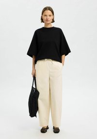 T-shirt noir oversized, pantalon large crème avec cordon, sac fourre-tout tissé noir, et chaussures à enfiler en maille noire. Tissu lisse, coupe décontractée.