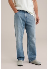 Lichtblauwe denim jeans met een relaxed fit, voorzien van een vijf-pocket ontwerp en subtiele vervaging. Draagt met een wit t-shirt en grijze klompen.