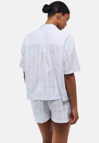 Chemise à manches courtes bleu clair à boutons et shorts assortis avec des rayures verticales. Confectionné dans un tissu léger avec une coupe décontractée.
