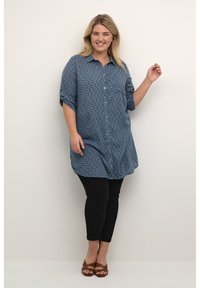 Niebieska koszula z krótkim rękawem w wzory, zestawiona z czarnymi spodniami slim-fit i brązowymi sandałami na paski.