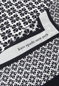 Sort og hvidt mønstret stof med blomster motiver, der har en kontrastkant og teksten "kate spade new york" i midten.