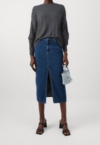 Grauer gerippter Pullover, knielanger Jeansrock mit vorderem Schlitz, schwarze Sandalen mit Blockabsatz und eine kleine hellblaue Handtasche mit Verzierungen.