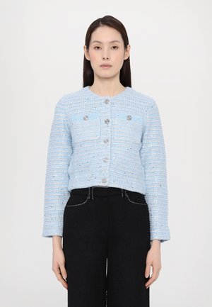 Sacou din tweed de culoare albastru deschis, cu guler rotund, buzunare frontale, nasturi argintii și mâneci lungi, purtat cu pantaloni negri cu talie înaltă.