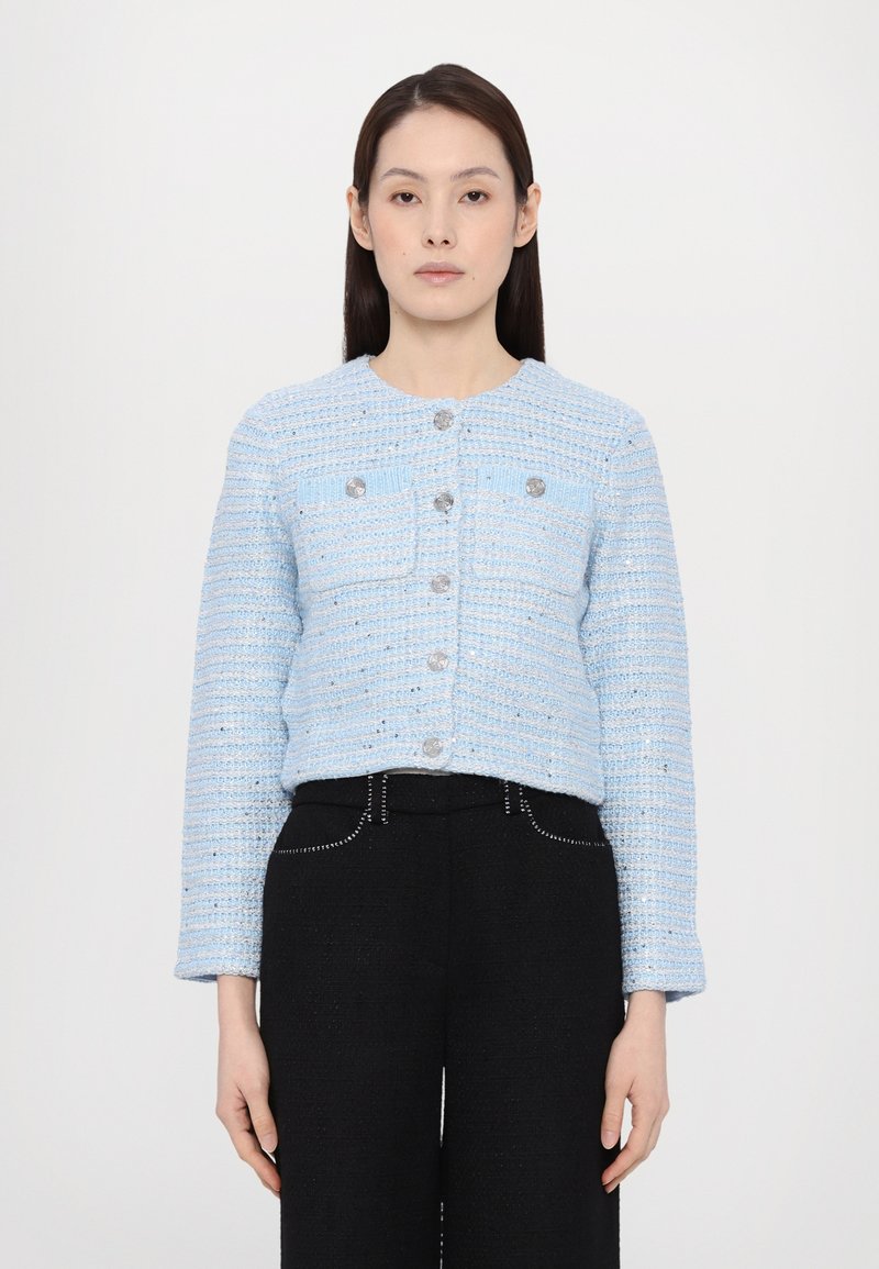 Light blue tweed jacket with a round neckline, front pockets, silver buttons, and long sleeves, paired with black high-waisted pants.